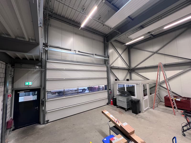 large industrial garage, roller door, metal ceiling, two waste bins, ladder