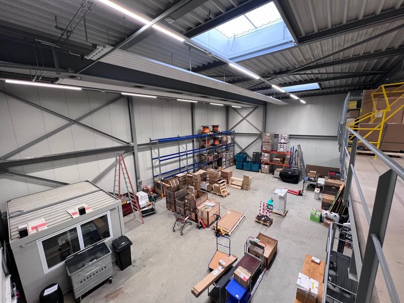 Empty industrial space with high ceiling, metal shelves, storage boxes, trolleys, and some tools, skylight in the ceiling
