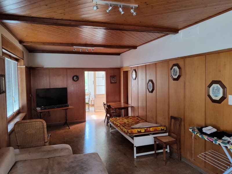 wooden walls, wooden floor, TV, coffee table, chairs, small bed, desk with television, ironing board, ironing table