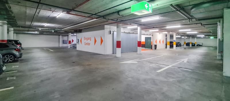 Underground parking garage with concrete floors, white walls, and signage indicating the entrance center. Several cars are parked in the space.