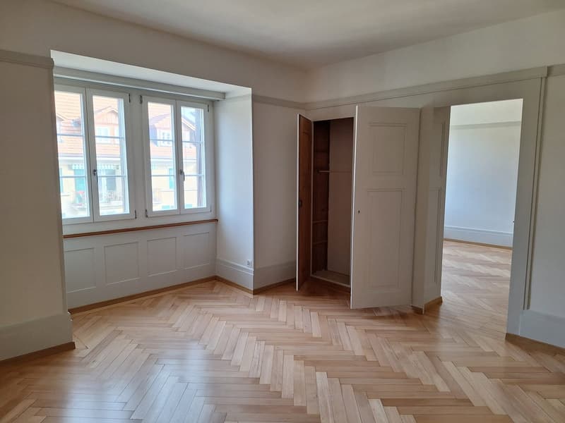 Empty room with wooden parquet flooring, white walls, large windows, and an open closet.