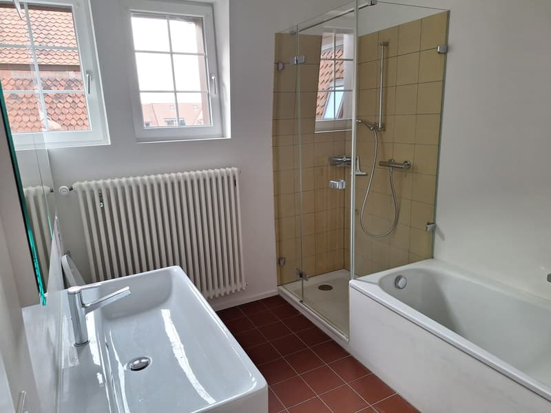 Bathroom with white sink, white bathtub, glass shower enclosure, tiled floor, radiator, window