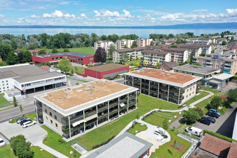 The image shows a residential area with multi-story apartment buildings, some with red roofs and others with green roofs. There are also some commercial or institutional buildings, including a large red building. The area has well-maintained green spaces