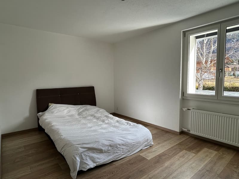 Empty bedroom with a bed, white walls, wooden floor, window with a view of the outside