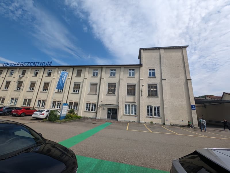 Industrial building, multiple parking places, a banner on the side, entrance in the middle, some windows, cars parked outside