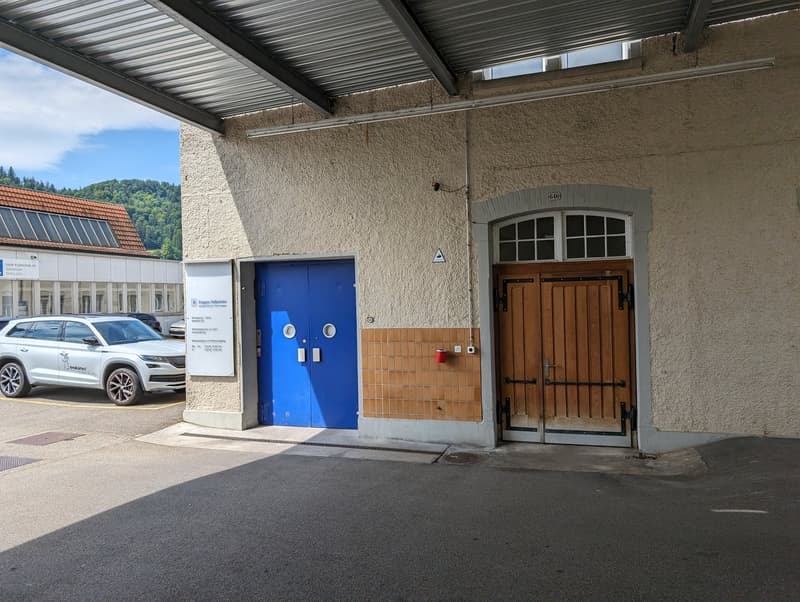 Building entrance, blue double doors, brown door, metal canopy, car parked in front, tiled wall section