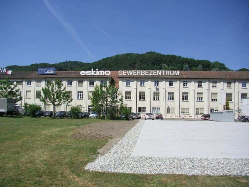 Office building, multiple windows, sign reads 'eskimo GEWERBEZENTRRUM', multiple cars parked in front, gravel driveway, grassy area in front