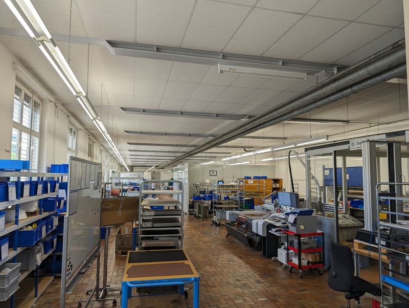 industrial area, fluorescent ceiling lights, brick floor, various storage racks, metal shelving, large cardboard boxes, multiple desks, machines and equipment