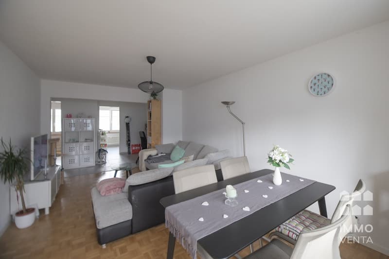 modern decor, open to dining area, grey couch with pillows, coffee table, floor lamp, desk with TV, white floor