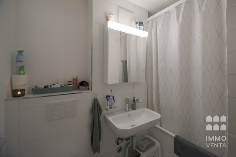 A bathroom with a modern design, featuring a sink, mirror, and white shower curtain, as well as storage space for toiletries. It includes a candle on the sink's surface.