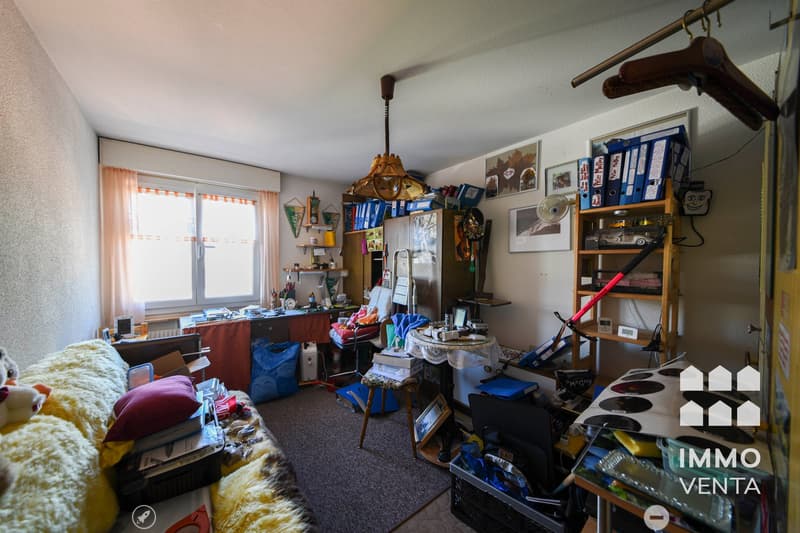 cluttered room with a desk, chair, shelves, and various items