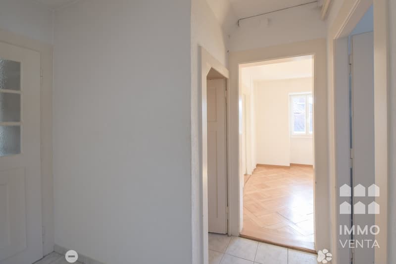 Empty room with white walls, wooden floor, and two doors leading to other rooms.