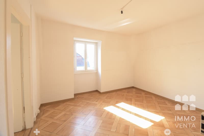 Empty room with wooden parquet floor, white walls, window, and sunlight