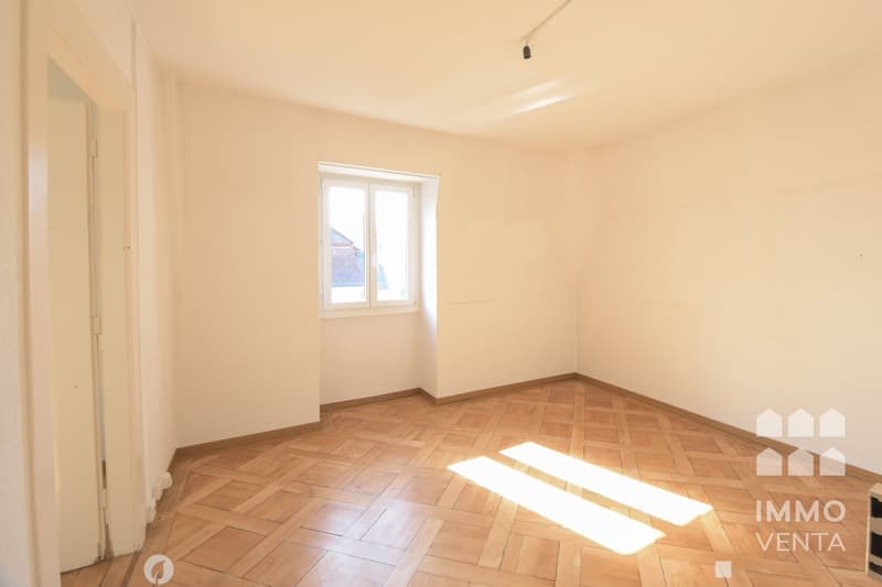 Empty room with wooden parquet floor, white walls, window, and sunlight