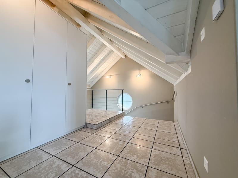 empty room with tiled floor, white walls, slanted ceiling, two white closets, window with a circular opening, a handrail on the wall