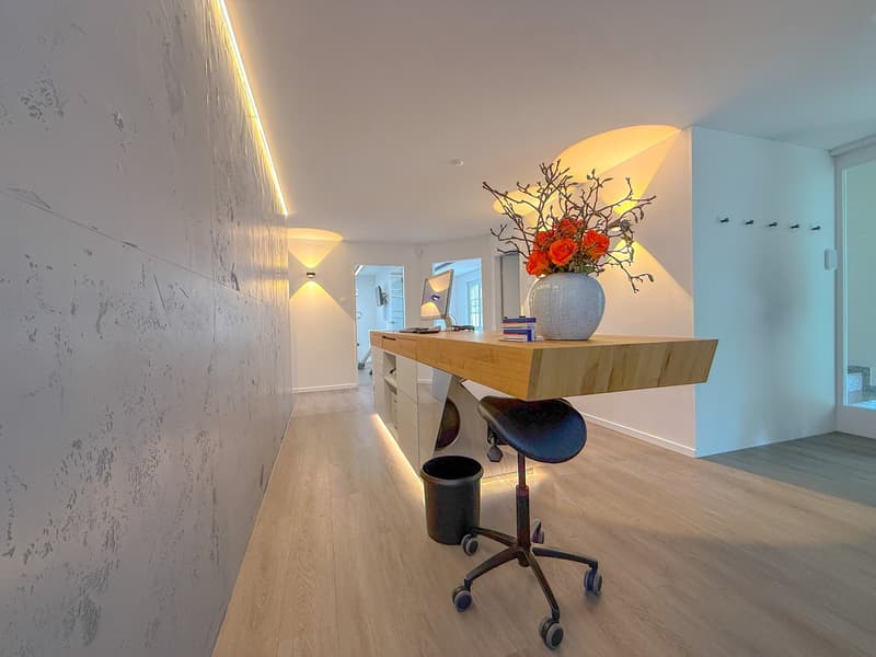 Wooden desk, vase with flowers, rolling chair, trash bin, monitor, cabinets, corridor