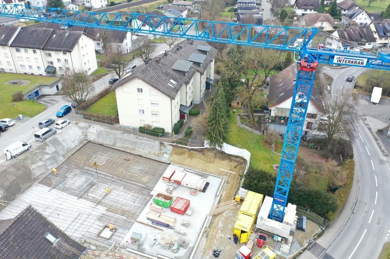 construction site with cranes, houses in the background, road, parked cars, and workers
