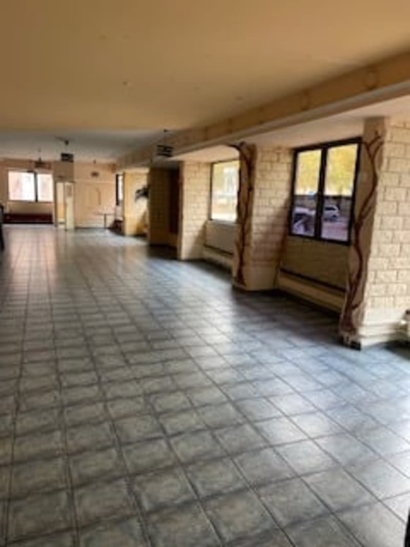 Empty room with tiled floor, brick walls, large windows, and a bench