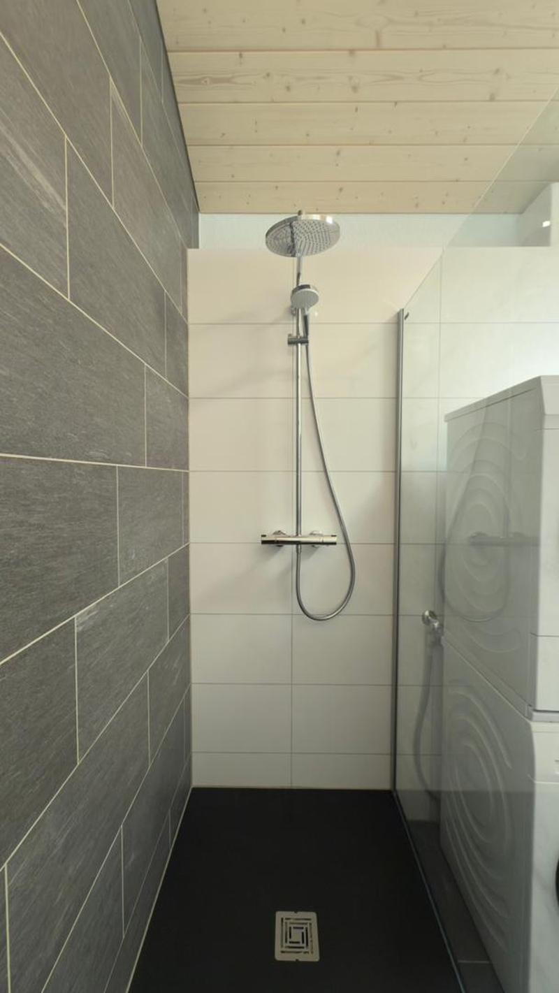 modern shower, tiled walls, black floor, glass door, washing machine