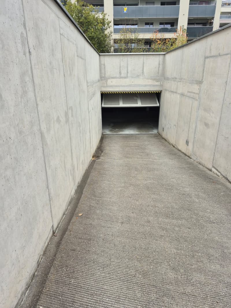 Concrete walkway leading to a garage entrance, surrounded by concrete walls.