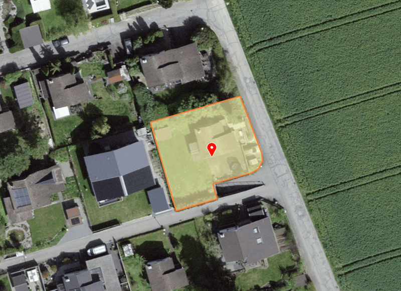Aerial view of a property, surrounded by houses, green grass, and a field