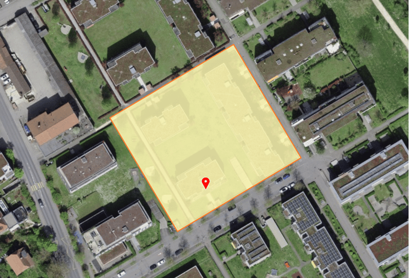 Aerial view of a rectangular plot of land with a red pin indicating the location, surrounded by buildings and greenery.