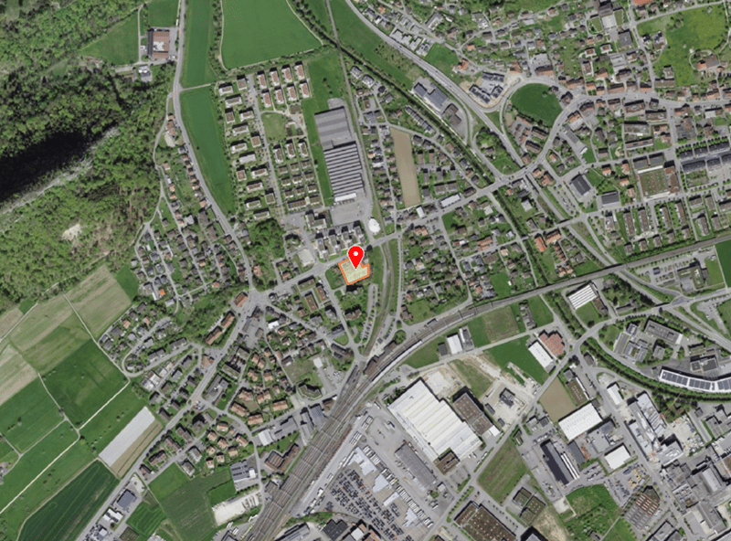 Aerial view of a town with residential and commercial buildings, green fields, and a railway station.