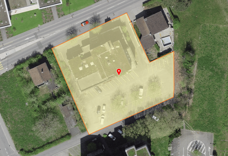 Building with parking lot, multiple cars parked, surrounded by grass and trees, road nearby