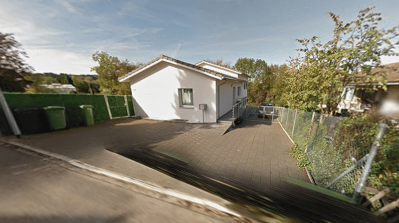 white house, raised ground floor, driveway, fence, green trash bins