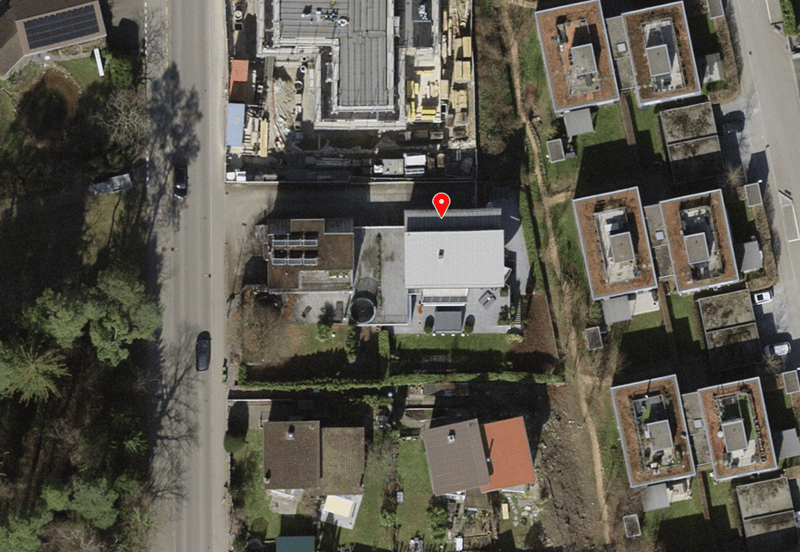 House with solar panels on the roof, surrounded by other houses and greenery, located on a street with parked cars.