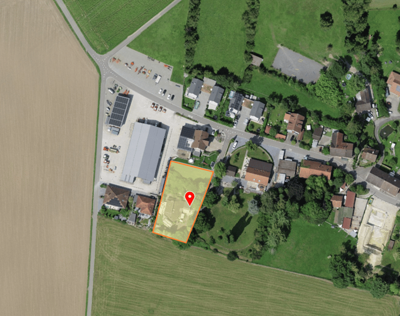 Aerial view of a rural area with a mix of residential and commercial buildings, a large field, and a road.