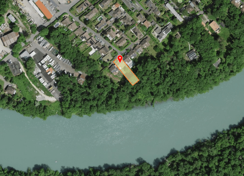 Aerial view of a property with a river and trees, located in a suburban area with several houses and buildings.