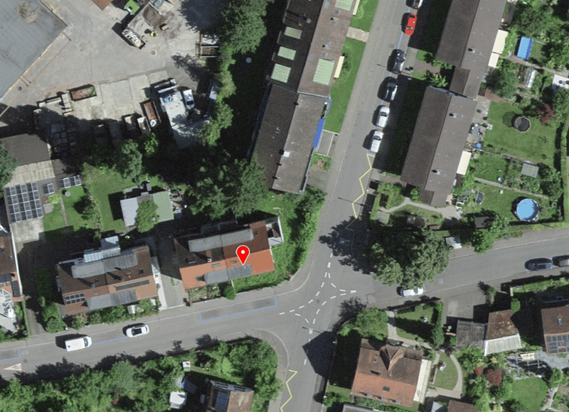 Aerial view of a neighborhood with several houses, a road, and a parking lot. Some houses have solar panels on their roofs.