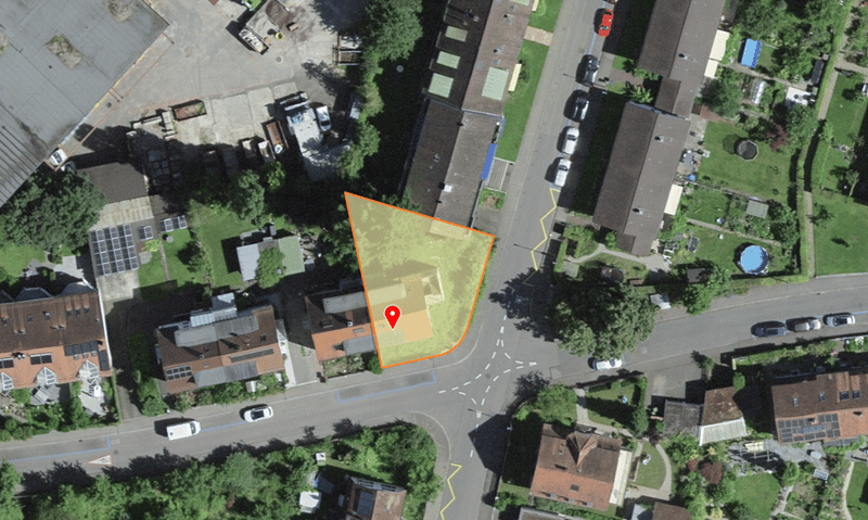 Aerial view of a residential area with several houses, a road, and a parking lot. The property is marked with an orange outline.