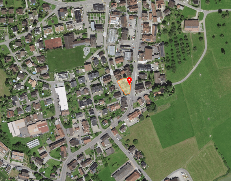 Aerial view of a neighborhood with residential buildings, green fields, and a road network.