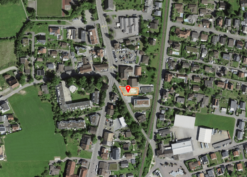 Aerial view of a residential area with various houses, a parking lot, and a building with a red marker.