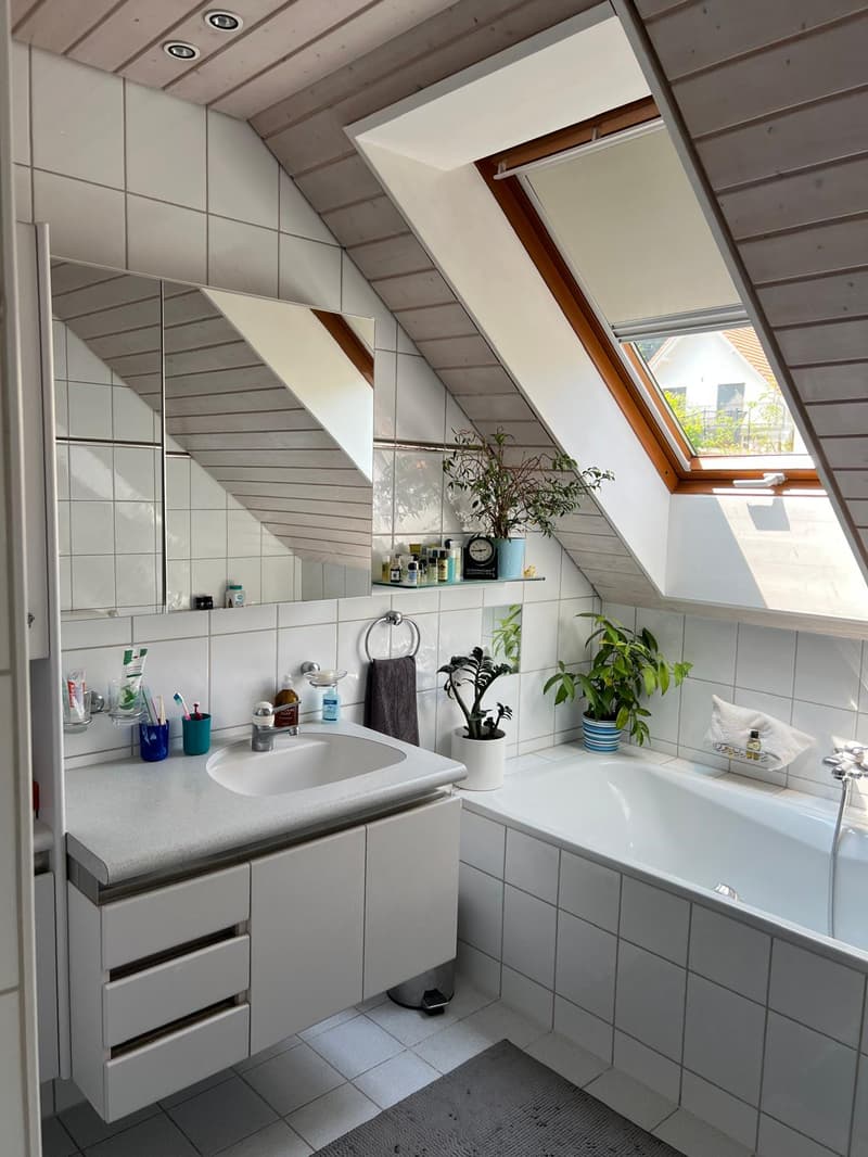 Bathroom with white tiles, bathtub, sink, mirror, plants, and a skylight window