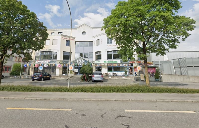 Buildings with restaurants, 2 cars parked, trees in front, road with lane markings