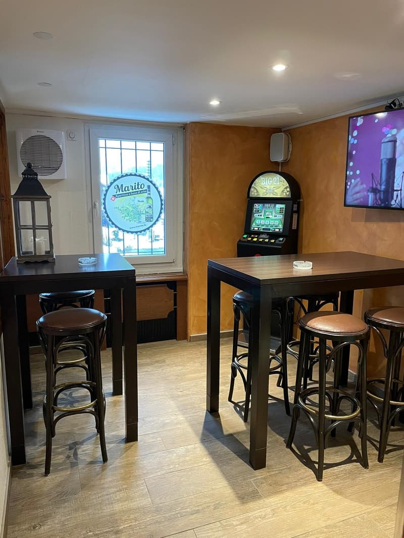 Room with two tables and bar stools, glass door, slot machine, screen, and air conditioning