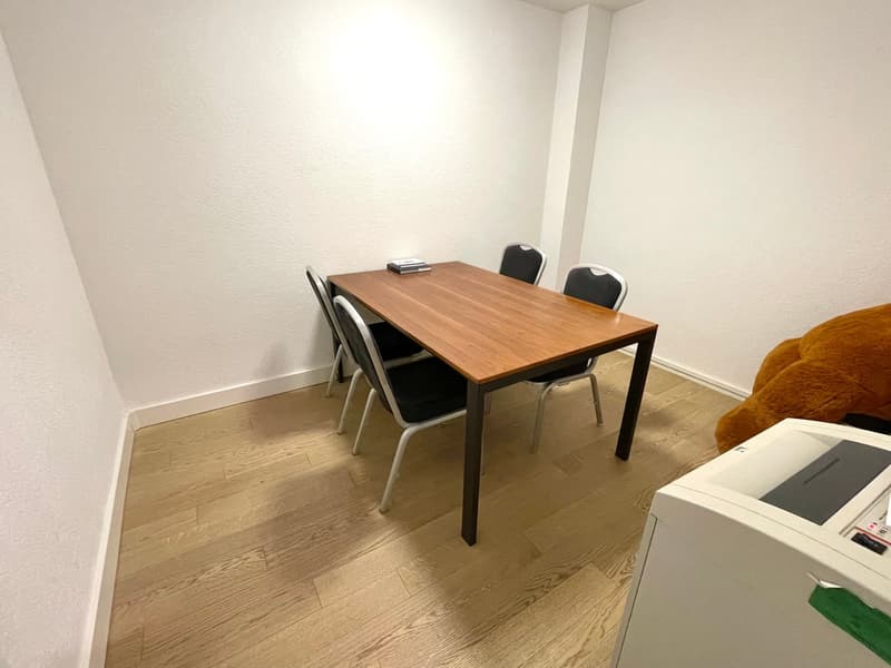 Small room with a wooden table and two black chairs, hardwood flooring, and a white wall.