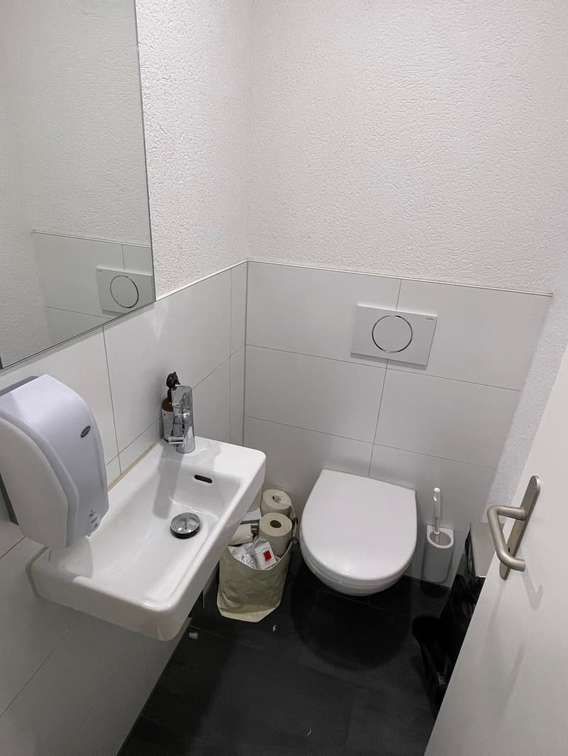 Small bathroom with white tiles, toilet, sink, and a washing machine