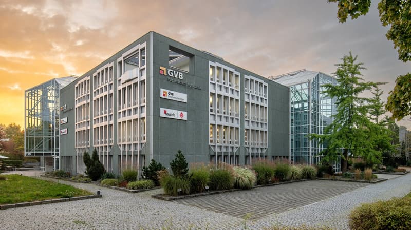 Modern office building with glass facades, multiple floors, and a paved entrance area.