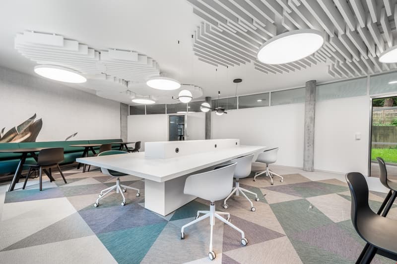 Modern office with a white long desk, various chairs, geometric carpet, round ceiling lights