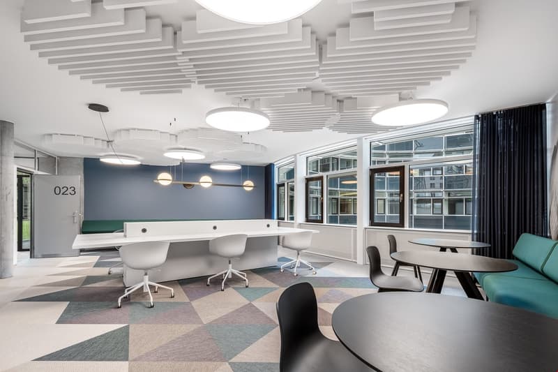 modern conference room, white and blue walls, large windows, geometric carpet, round tables, green couch, modern lighting