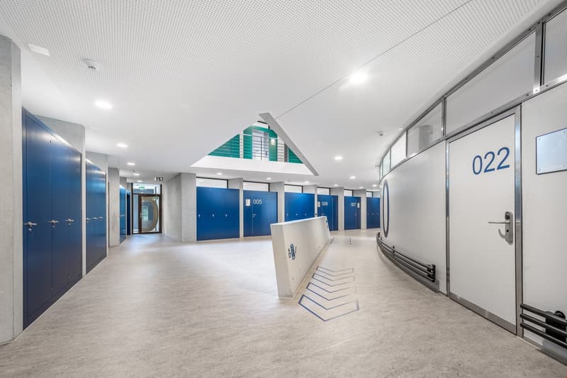 blue storage doors, arched metal beam in ceiling, gray floor, white wall, room numbers on doors