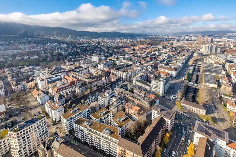 Aerial view of a city with many buildings, roads, and greenery, mountains in the distance