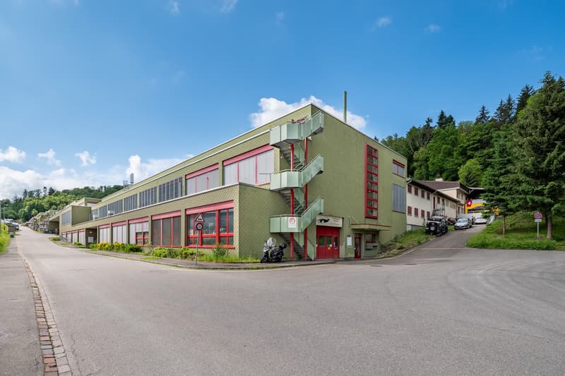 Modern building with green exterior and red trim, staircase leading up to second floor, industrial windows, motorcycles parked in front