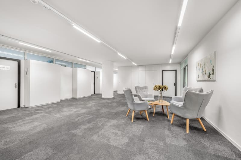 Empty meeting room with grey chairs, wooden coffee table, flowers in vase, white walls and ceiling, white doors