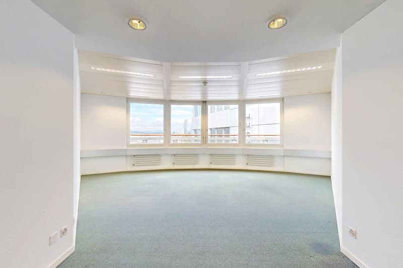 Large, open room with curved windows providing a panoramic view, white walls, recessed lighting, and a tiled floor.