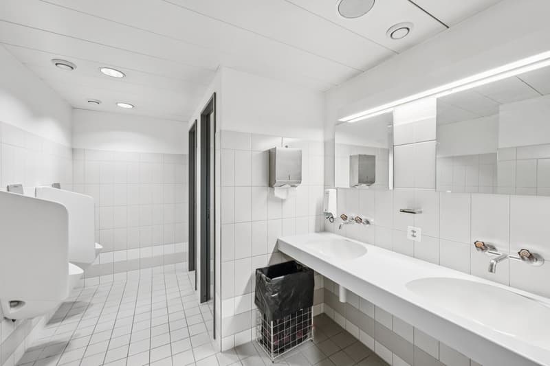 modern and minimalist bathroom with white tiles, two urinals, one washbasin, and a trash bin